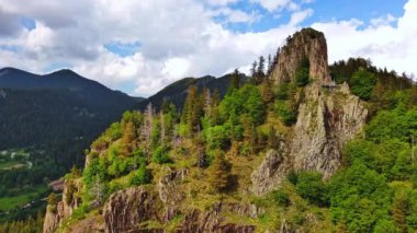 High rocky wild mountain range of Rhodope Mountains covered with green vegetation, against backdrop of mountain valley covered with dense dark spruce forests and blue cloudy sky. UHD 4K video realtime