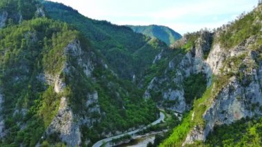 Dar, dolambaçlı bir dağ yolu, Rodop Dağları 'ndaki mavi bulutlu bir gökyüzünün altında yeşil yay dağ bitkilerinin bulunduğu dağ kanyonlarından geçer. UHD 4K video gerçek zamanlı