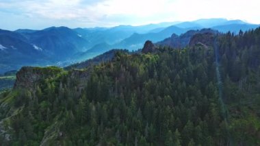 High rocky wild mountain range of Rhodope Mountains covered with green vegetation, against backdrop of mountain valley covered with dense dark spruce forests and blue cloudy sky. UHD 4K video realtime