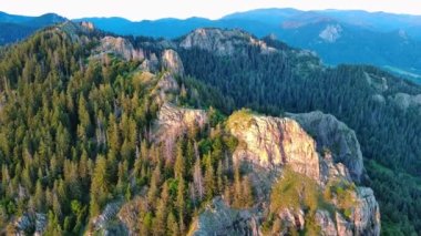 High rocky wild mountain range of Rhodope Mountains covered with green vegetation, against backdrop of mountain valley covered with dense dark spruce forests and blue cloudy sky. UHD 4K video realtime