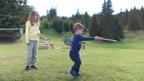 今年春天 一位穿着黄色运动服的大姐和弟弟一起玩耍 教他如何在后院的绿色草坪上吹肥皂泡 Uhd Video慢动作4K — 图库视频影像