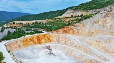 A natural stepped quarry rich in minerals is located near winding road, against backdrop of Rhodope Mountains and hills with evergreen spruce forests and mountain vegetation. UHD 4K video realtime