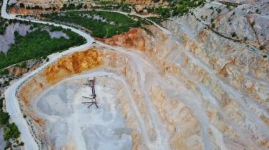 A natural stepped quarry rich in minerals is located near winding road, against backdrop of Rhodope Mountains and hills with evergreen spruce forests and mountain vegetation. UHD 4K video realtime