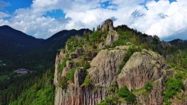 High rocky wild mountain range of Rhodope Mountains covered with green vegetation, against backdrop of mountain valley covered with dense dark spruce forests and blue cloudy sky. UHD 4K video realtime