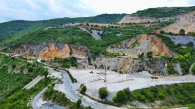 Industrial quarry for extraction of minerals with equipment and machines, and intermountain winding road passing by, in Rhodope Mountains covered with coniferous forests. UHD 4K video realtime