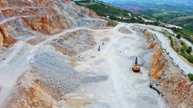 A natural stepped quarry rich in minerals is located near winding road, against backdrop of Rhodope Mountains and hills with evergreen spruce forests and mountain vegetation. UHD 4K video realtime