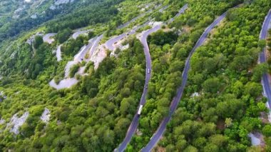 İnanılmaz dolambaçlı dağ yolu - Lovcensky keskin virajlarıyla Karadağ 'ın yeşil bitki örtüsüyle kaplı dağlarının zirvesine çıkıyor. UHD Video gerçek zamanlı 4K