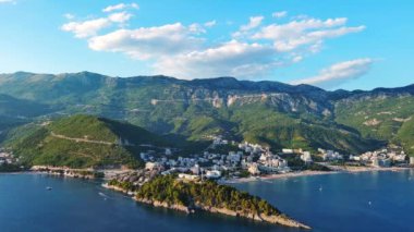 Budva ve Becici tatil beldeleri, sakin Adriyatik Denizi yakınlarında lüks oteller ve rahat plajlarla Karadağ Dağları ve mavi gökyüzüne karşı. UHD Video gerçek zamanlı 4K