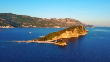 Adriyatik Denizi kıyılarında bitki örtüsü bulunan tarihi antik St. Nicholas adası kıyı kentleri, Karadağ dağları ve açık gökyüzü karşısında yer alıyor. UHD Video gerçek zamanlı 4K