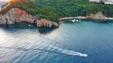 Gezintiler için küçük beyaz bir motorlu tekne yüksek tehlikeli uçurum yamaçlarının altında turkuaz deniz suyunda yüzüyor. UHD Video gerçek zamanlı 4K