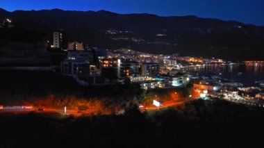 Karadağ dağlarının yamaçlarına ve Adriyatik Denizi yakınlarındaki yıldızlı karanlık gökyüzüne karşı renkli elektrik ışıkları ve plajları olan bir turizm şehri. UHD Video gerçek zamanlı 4K