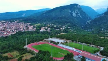 Yunanistan 'ın Litochoro kenti yakınlarındaki spor sahası ve futbol sahası, yüksek seviyeli Olimpos Dağı ve bulutlu gökyüzünün arka planına karşı yeşil bitki örtüsüyle kaplı. UHD Video gerçek zamanlı 4K
