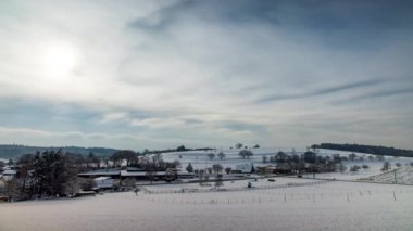 Kar, eski küçük bir köyü ahşap evler ve tarım çiftlikleri ile kapladı. Kel ağaçlarla kaplı tepelik bir bölgede kış bulutlu havalarda. Video 4K UHD zaman ayarlı