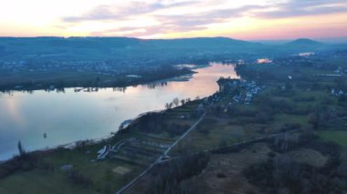 Yeşil tarlalar ve çayırlar, ormanlık tepeler ve dağlar, küçük köyler ve çiftlikler ve geniş yansıtıcı nehir Rhine üzerinde sihirli bulutlu bir akşam gökyüzü. 4K UHD video gerçek zamanlı