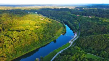 Kupa nehri, Hırvatistan ve Slovenya 'nın yeşil yaprak döken ormanları arasında güneşli bir gökyüzü ve dağların arka planına karşı otoyolun yanında akar. 4K UHD video gerçek zamanlı