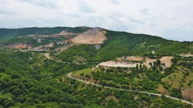 Industrial quarry for extraction of minerals with equipment and machines, and intermountain winding road passing by, in Rhodope Mountains covered with coniferous forests. UHD 4K video realtime