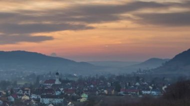 Ren nehrinin kıyısındaki küçük bir dağ kasabasında güneşli ve bulutlu bir gün batımı ve orman doğasında antik binalar. Video 4K UHD zaman ayarlı