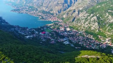 Deniz ünlü Kotor Koyu tatil köyü plajları ve otelleri, açık mavi güneşli gökyüzünün zeminine karşı Karadağ dağlarının gölgesindeki gök mavisi Adriyatik Denizi. UHD Video gerçek zamanlı 4K