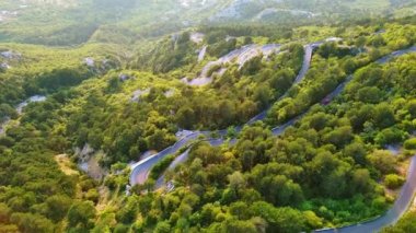 İnanılmaz dolambaçlı dağ yolu - Lovcensky keskin virajlarıyla Karadağ 'ın yeşil bitki örtüsüyle kaplı dağlarının zirvesine çıkıyor. UHD Video gerçek zamanlı 4K