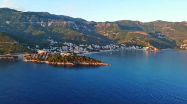 Budva ve Becici tatil beldeleri, sakin Adriyatik Denizi yakınlarında lüks oteller ve rahat plajlarla Karadağ Dağları ve mavi gökyüzüne karşı. UHD Video gerçek zamanlı 4K