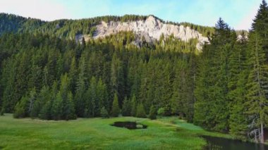 Işıl ışıl parlayan berrak göl, berrak mavi bulutlu bir gökyüzüne, yeşil ağaçlık dağ sıralarına ve küçük çiftçi dağ köylerine karşı parlak sıcak güneş ışığını yansıtır. UHD 4K video gerçek zamanlı