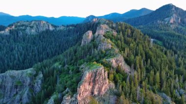 High rocky wild mountain range of Rhodope Mountains covered with green vegetation, against backdrop of mountain valley covered with dense dark spruce forests and blue cloudy sky. UHD 4K video realtime