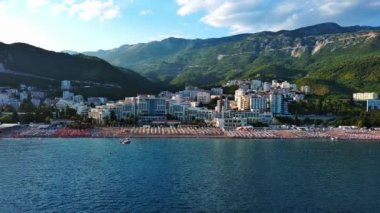 Budva ve Becici tatil beldeleri, sakin Adriyatik Denizi yakınlarında lüks oteller ve rahat plajlarla Karadağ Dağları ve mavi gökyüzüne karşı. UHD Video gerçek zamanlı 4K