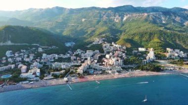 Budva ve Becici tatil beldeleri, sakin Adriyatik Denizi yakınlarında lüks oteller ve rahat plajlarla Karadağ Dağları ve mavi gökyüzüne karşı. UHD Video gerçek zamanlı 4K