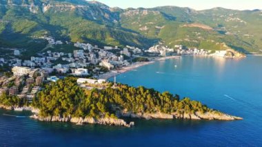 Budva ve Becici tatil beldeleri, sakin Adriyatik Denizi yakınlarında lüks oteller ve rahat plajlarla Karadağ Dağları ve mavi gökyüzüne karşı. UHD Video gerçek zamanlı 4K