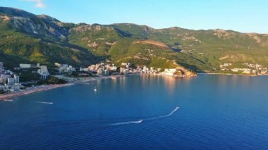 Budva ve Becici tatil beldeleri, sakin Adriyatik Denizi yakınlarında lüks oteller ve rahat plajlarla Karadağ Dağları ve mavi gökyüzüne karşı. UHD Video gerçek zamanlı 4K