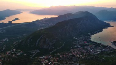 Mavi bulutlu gökyüzünde parlayan yaz güneşi Karadağ dağlarının siluetlerini ve ünlü Kotor Körfezi kıyılarını aydınlatıyor. UHD Video gerçek zamanlı 4K