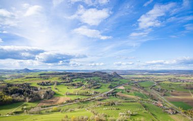 Otoyolları ve yolları olan küçük bir Avrupa kasabası, tarım arazileri, ormanlı karanlık tepe siluetleri ve güneşli bir akşam gökyüzü karşısında çiftçi otlakları
