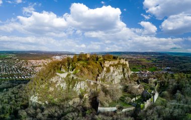 Üzerinde tarihi Hohentwil şatosunun kalıntıları olan yüksek yeşil ağaçlık bir tepenin panoraması güneş ışığında parlak mavi bir gökyüzüne karşı.