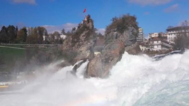 Hızlı fırtınalı soğuk su damlaları düşer ve küçük damlalar Rhine Şelaleleri 'ne İsviçre' deki eski kasabanın arka planına doğru farklı yönlere dağılır. 4k video yavaş çekim UHD