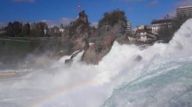 Hızlı fırtınalı soğuk su damlaları düşer ve küçük damlalar Rhine Şelaleleri 'ne İsviçre' deki eski kasabanın arka planına doğru farklı yönlere dağılır. 4k video yavaş çekim UHD