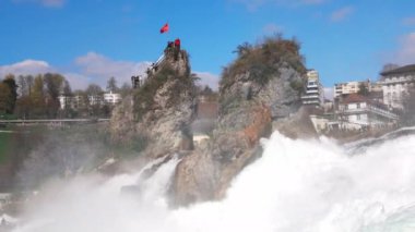 Hızlı fırtınalı soğuk su damlaları düşer ve küçük damlalar Rhine Şelaleleri 'ne İsviçre' deki eski kasabanın arka planına doğru farklı yönlere dağılır. 4k video yavaş çekim UHD
