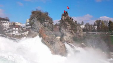 Hızlı fırtınalı soğuk su damlaları düşer ve küçük damlalar Rhine Şelaleleri 'ne İsviçre' deki eski kasabanın arka planına doğru farklı yönlere dağılır. 4k video yavaş çekim UHD