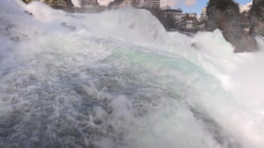Hızlı fırtınalı soğuk su damlaları düşer ve küçük damlalar Rhine Şelaleleri 'ne İsviçre' deki eski kasabanın arka planına doğru farklı yönlere dağılır. 4k video yavaş çekim UHD
