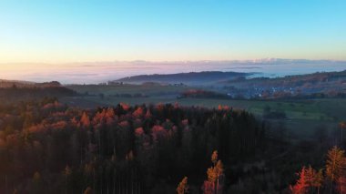 Yoğun karanlık çam ormanlarıyla dağ vadisi, boş çim tarlaları ve akşam güneşinde karla kaplı yüksek dağlara bakan küçük köyler. Video 4k UHD eş zamanlı