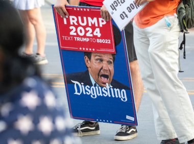 Milwaukee, Wisconsin, USA - August 23, 2023: A supporter of President Joe Biden holds a protest sign against Florida Governor Ron Desantis at the entrance to the first 2024 Republican Presidential Debate. clipart