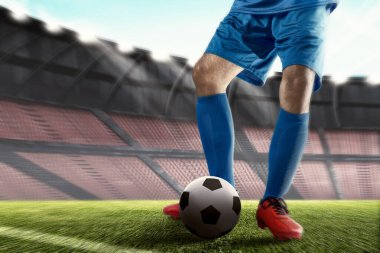 Futbol oyuncusu mavi formalı adam elinde topla futbol sahasında duruyor.