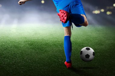 Mavi formalı bir futbolcunun futbol sahasında topa vuruşunun arka görüntüsü.