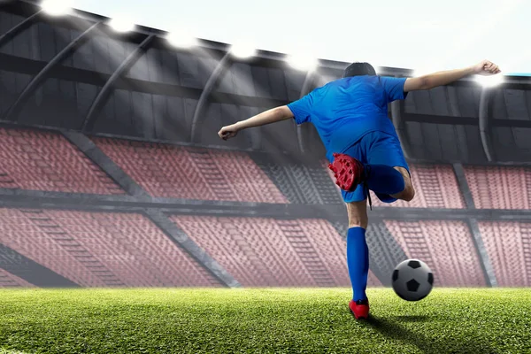 一个身穿蓝色球衣的足球运动员在足球场上踢球的背影 — 图库照片
