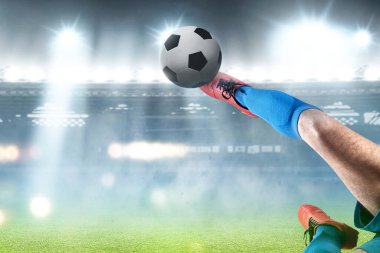 Mavi formalı bir futbolcu futbol sahasında topa vuruyor.