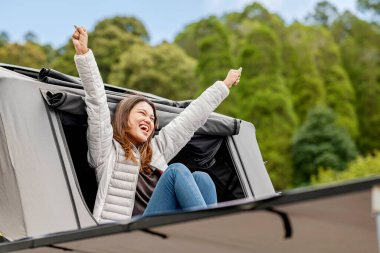 Karavanın üstündeki çadırın dışında oturan Asyalı kadın doğada kamp faaliyetlerinin keyfini çıkarıyor.