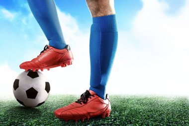 Futbol oyuncusu mavi formalı adam elinde topla futbol sahasında duruyor.