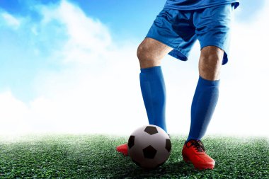 Mavi formalı bir futbolcu futbol sahasında topa vuruyor.