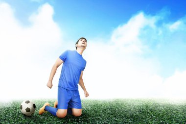 Mavi formalı Asyalı futbolcu futbol sahasındaki zaferini kutluyor.