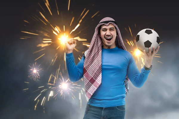 Azjata Keffiyeh Stoi Trzymając Piłkę Szczęśliwym Wyrazem Twarzy Tle Fajerwerków — Zdjęcie stockowe