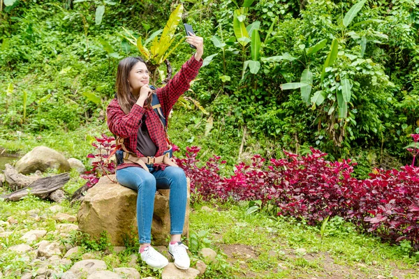 森の中で携帯電話で自画像を撮るバックパックを持つアジアの女性 — ストック写真